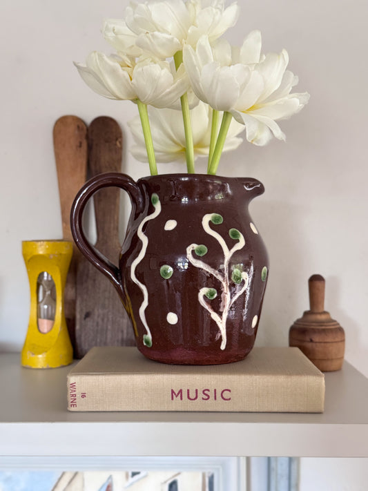 Brown ceramic pitcher with green and white design on a book with 'Music' on a shelf.